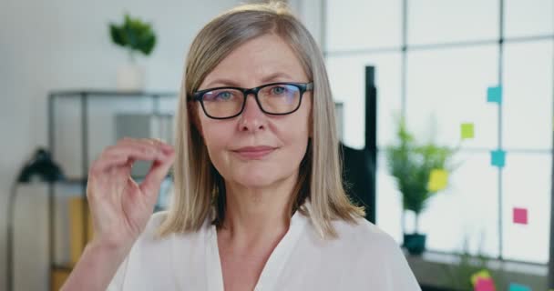 Zbliżenie się z uroczy pewny siebie blondynka dorosłych businesswoman który zdejmuje jej okulary podczas patrząc w aparat z szczęśliwy wyraz twarzy w biurze — Wideo stockowe