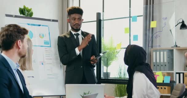 Ελκυστικός χαμογελαστός επιτυχημένος μαύρος-ξεφλουδισμένος αρσενικός ηγέτης που κατέχει επιχειρηματική κατάρτιση για διάφορους εταιρικούς συναδέλφους στο σύγχρονο γραφείο — Αρχείο Βίντεο