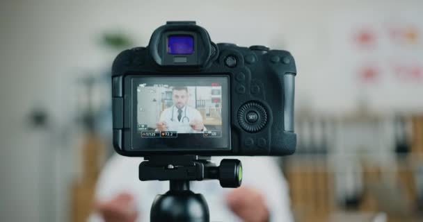 Vue à travers la caméra sur médecin barbu moderne confiant et hautement qualifié qui montre à l'audience Internet comment utiliser un masque de protection pour se protéger contre le coronavirus — Video