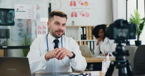 Sonriente simpático satisfecho médico barbudo altamente cualificado aplaudiendo las manos después de terminar su chat de vídeo médico a través de la cámara con la audiencia en línea, cámara lenta — Vídeos de Stock