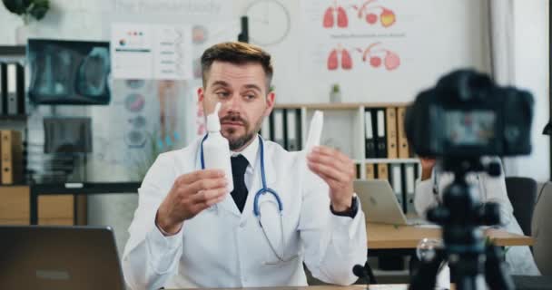 Aantrekkelijk zelfverzekerde gekwalificeerde bebaarde arts neemt videvlog op camera op en vertelt zijn publiek over medicijnen, medicijnen en blogging concept — Stockvideo