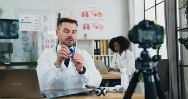 Concepto de telemedicina donde el médico barbudo inteligente y atractivo explica a través de la cámara cómo usar el oxímetro de pulso — Vídeos de Stock