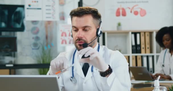 Sluiten van een goed uitziende, zelfverzekerde, moderne medisch specialist met baarden voor volwassenen in headsets die online een vergadering op de computer houdt en met collega 's discussieert over de noodzaak van vaccinatie — Stockvideo