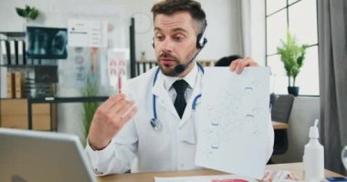 Kendine güveni tam profesyonel sakallı doktor elinde video görüntülü konuşma ve izleyiciler için kimyasal formülü dizüstü bilgisayarla açıklıyor.