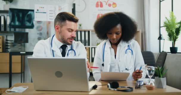 Концепция медицины, где привлекательные положительные разнообразные два высококвалифицированных врача-мужчины и женщины работают вместе с отчетами и информацией в ноутбуке в медицинской лаборатории — стоковое видео