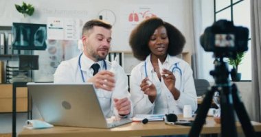 Sağlık kanalı için video bloğu kaydeden ve birlikte antibakteriyel spreyler sergileyen başarılı, başarılı, çok ırklı kadın ve erkek doktorlar var.