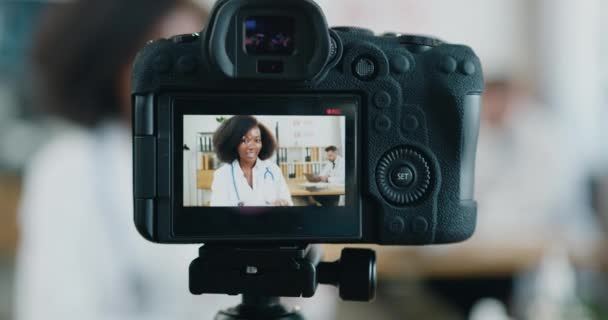 Záznam na profesionální fotoaparát krásné pozitivní zkušené černošky-kůže lékaře, který streaming konverzace z lékařské laboratoře v blízkosti tvrdě pracuje na notebook vousatý mužský kolega — Stock video