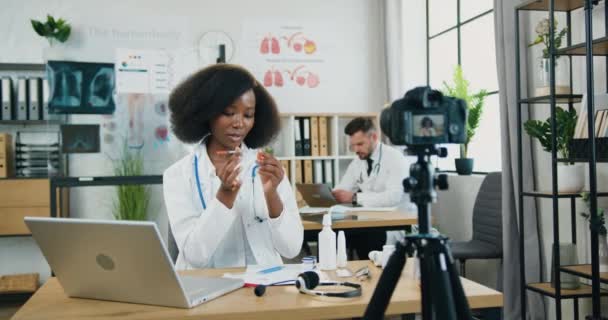 Mooie zelfverzekerde positieve ervaren zwarte huid vrouwelijke arts opnemen video voor internet publiek en vertellen hoe u vaccin spuit te gebruiken — Stockvideo