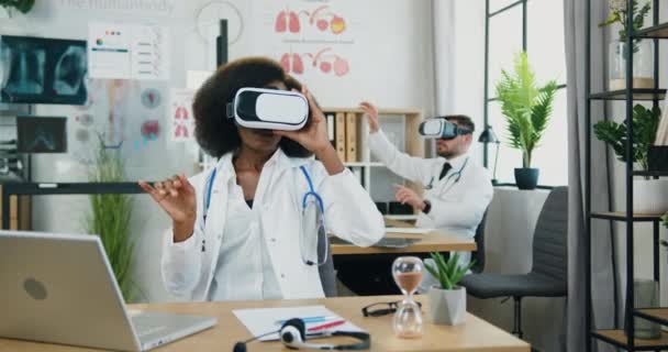 Dobrze wyglądający, skoncentrowany nowoczesny, wysoko wykwalifikowany lekarz rasy męskiej i żeńskiej pracujący razem w virtaul reality headsets w gabinecie medycznym — Wideo stockowe