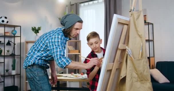 Atractivo creativo joven artista masculino enseñando a un niño pequeño a dibujar en el taller, concepto de arte — Vídeo de stock