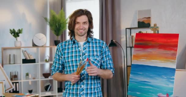 Close up of likable smiling confident skilful modern young male artist which posing on camera in home studio and gesturing thumb up,arts concept — Stock Video