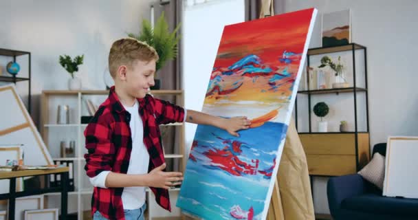 Modern artwork concept where attractive happy interested schoolboy painting with hands on canvas applying colourful strokes in workshop — Stock Video