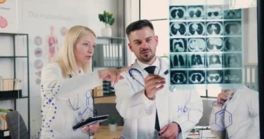 Tıp konsepti. Çekici, deneyimli erkek ve kadın doktorların tıp laboratuarında birlikte çalışıp hastaların röntgenlerini tartışmaları.