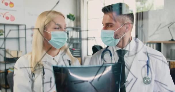 Attractive successful qualified two doctors-man and woman in protective masks discussing results of scull scan and consulting about future treatment of patient — Stock Video
