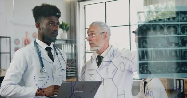 Atrakcyjne poważnie szanowany wykwalifikowany brodaty profesor Uniwersytetu Medycznego rozmawia ze swoim pewnym siebie afrykańskim studentem w laboratorium klinicznym i wyjaśnia skan rentgenowski — Wideo stockowe