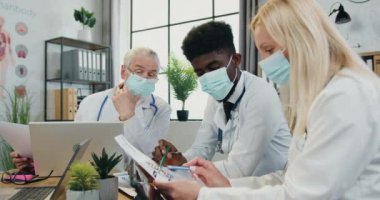 Coronavirus pandemisi sırasındaki tıbbi toplantı. Klinikteki danışmanlık sırasında maskeli başarılı başarılı erkek ve kadın doktorlar tıbbi anlarını tartışıyor.