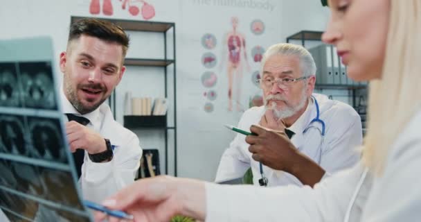 Koncepcja medycyny, gdzie sympatyczny pewny siebie wykwalifikowanych trzech lekarzy omawiających obraz rentgenowski pacjentów podczas wspólnego spotkania w biurze medycznym — Wideo stockowe