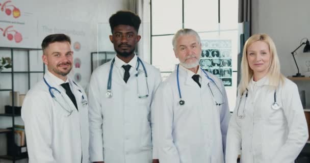 Portrait de bonne mine positive confiant expérimenté équipe médicale diversifiée en manteaux blancs qui se tient devant la caméra avec les bras croisés dans le bureau de la clinique moderne — Video