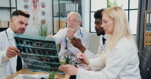 Gradevole fiducioso esperto gruppo di medici che discutono pazienti radiografia insieme con il loro rispettato medico capo barbuto durante il briefing congiunto in aula operatoria — Video Stock