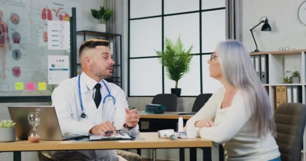 Concepto de medicina donde atractiva mujer mayor de cabello gris responsable visita a su médico de familia en el consultorio de la clínica moderna — Vídeo de stock