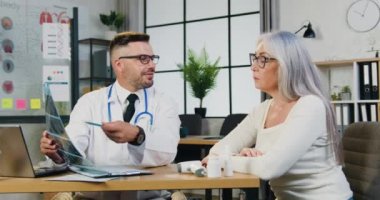 Kendine güveni tam, özenli, sakallı bir doktor. Klinikteki muayenesi sırasında konsantre olmuş güzel bayan hastasına röntgen sonuçlarını açıklıyor.