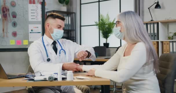 얼굴 마스크를 쓴 유능 한 남성 의사가 여성 환자의 손목 맥박을 체크하고 리듬을 세는 의학 센터의 약속 — 비디오