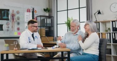 Tıp konsepti. Yakışıklı, deneyimli, sakallı bir doktorun kliniğe giderken olgun bir aile çiftiyle gülümsemesi. Kapatın.