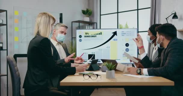 Företag under coronavirus pandemi där attraktiva ansedda erfarna blandras företagare i ansiktsmasker brainstorming tillsammans i styrelserummet om gemensam strategi — Stockvideo