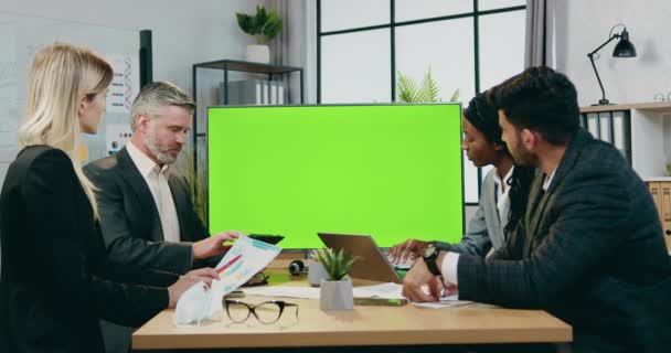 Aantrekkelijk zelfverzekerd succesvolle ervaren multiraciale mannelijke en vrouwelijke zakenpartners die samenwerken in moderne directiekamer nabij groen chroma-scherm — Stockvideo