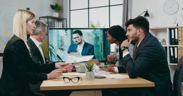 Хорошо выглядящие успешные опытные бизнесмены смешанной расы проводят онлайн-конференцию со своим коллегой-мужчиной во время встречи в современном зале заседаний — стоковое видео