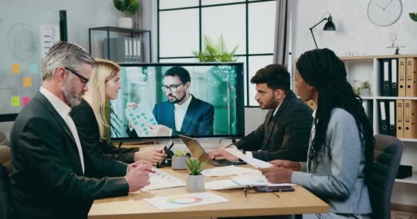 Attraktiv positiv erfaren blandras företagare har videokonferens med sin manliga kollega på tv under mötet i moderna styrelserummet — Stockvideo