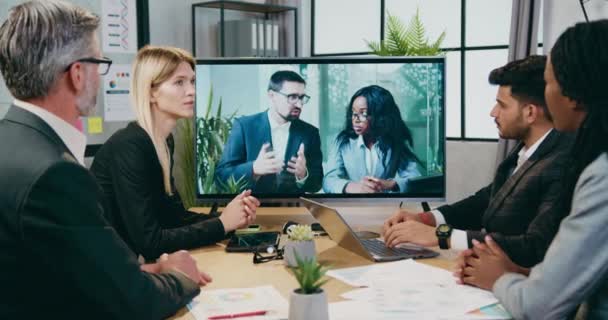 Boa aparência profissional inteligente experiente mestiço empresários aconselhando entre si durante videoconferência com seus parceiros internacionais masculinos e femininos na tv no escritório — Vídeo de Stock