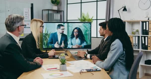 Närbild av snygg självsäker kvalificerad multiracial företagare som sitter i styrelserummet under konferens chatt möte med manliga och svarthyade kvinnliga kollegor — Stockvideo