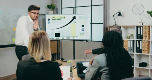 Conceito de negócio onde atraente confiante homem de negócios barbudo qualificado explicando a apresentação no quadro branco para diversos colegas corporativos motivados qualificados durante a reunião — Vídeo de Stock