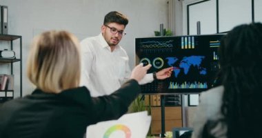 İyi görünümlü, kendine güvenen, yüksek yetenekli, sakallı iş adamı ortak toplantıda başarılı uluslararası meslektaşları için dijital ekranda sunumu açıklıyor.