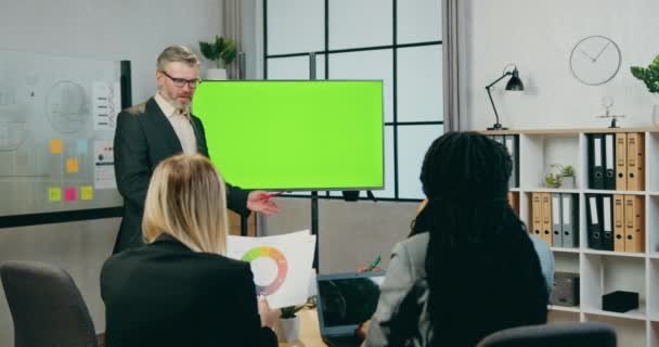 Aantrekkelijk zelfverzekerde ervaren bebaarde zakenman in gesprek met succesvolle gemengde ras mannelijke en vrouwelijke collega 's, terwijl hij in de buurt van groen scherm in bestuurskamer — Stockvideo