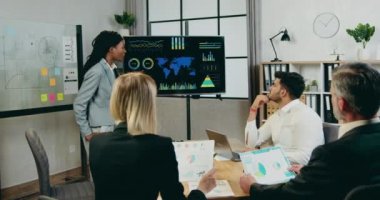 Güzel, kendine güvenen, siyah tenli bir kadının ortak toplantı sırasında dijital ekranda karışık motivasyonlu melez ırk meslektaşlarına rapor verdiği iş konsepti.