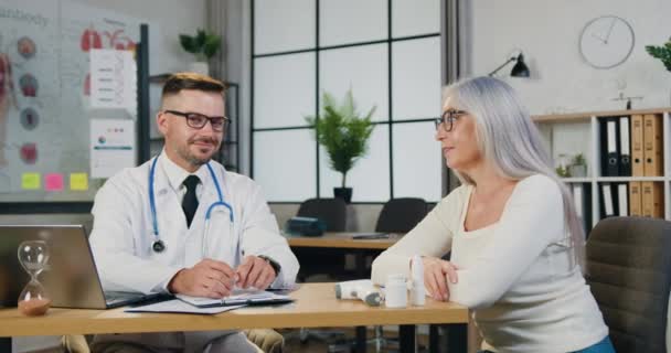 Mulher de meia-idade com médico assistente sorrindo olhando para a câmera durante o tratamento bem sucedido consulta médica. Conceito de recuperação de cuidados de saúde para idosos — Vídeo de Stock