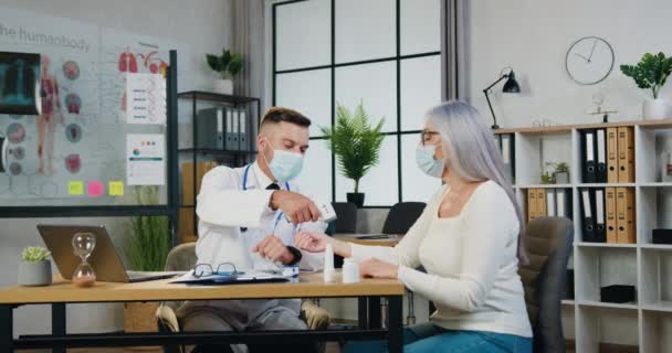 Medico concentrato in maschera protettiva che misura la temperatura di una paziente anziana con termometro a infrarossi in clinica. Concetto sanitario e medico — Video Stock