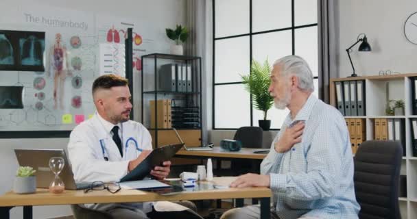 Gericht gezondheidswerker noteert de medische geschiedenis en klachten van een oudere man tijdens een bezoek aan de arts in de kliniek. Gezondheidsconcept — Stockvideo
