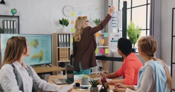 Atraente concentrou sucesso diversificada equipe feminina observando como seu colega escrevendo notas em placa de vidro durante reunião conjunta sobre estratégia de negócios — Vídeo de Stock