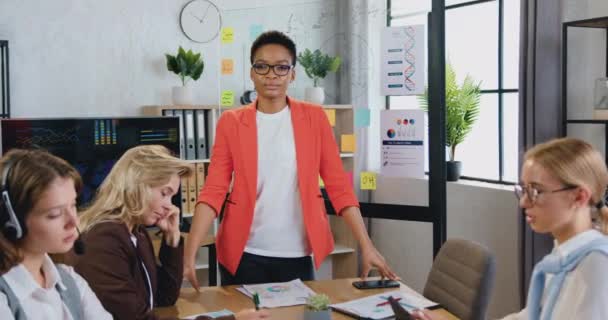 Porträtt av snygg leende framgångsrik skicklig affärskvinna i glasögon som poserar på kameran i kontorsrum nära arbetande kvinnliga kollegor — Stockvideo