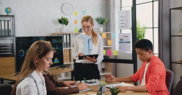 Ritratto di attraente sorridente giovane donna qualificata di successo che lavora su tablet pc e guarda nella fotocamera mentre le femminili- colleghi brainstorming sul posto di lavoro in ufficio — Video Stock