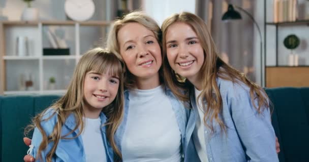 Close-up portret van mooie glimlachen gelukkig blond moeder en haar schattige vriendelijke jongere en oudste dochters die op zoek naar camera met knuffels thuis — Stockvideo