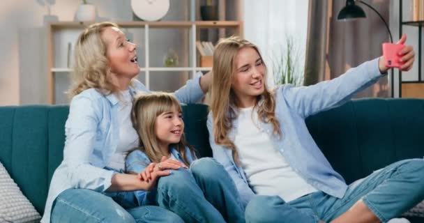 Familie concept waar aantrekkelijke positieve zorgeloze vrolijke vriendelijke vrouw en haar dochters genieten van videogesprek met familieleden op mobiel thuis, front view — Stockvideo