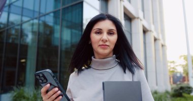 İnternette akıllı telefon kullanan, gülümseyen kameraya bakan güzel beyaz bir kadının yakın görüntüsü. Portre konsepti. Açık havada.
