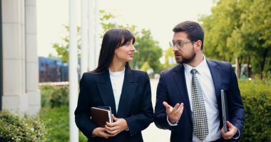 Mutlu iş arkadaşları, resmi takım elbiseli bir adam ve bir kadın, kentin bir bölgesinde yürüyorlar, işe giderken, dizüstü bilgisayar taşıyan bir kadınla sohbet ediyorlar.
