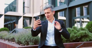Odaklanmış olgun bir adam ofis binasının dışına çıkıyor online toplantı yapıyor, orta yaşlı bir iş adamı video görüşmesi yaparken dizüstü bilgisayarla yürüyor. Yavaş çekim.