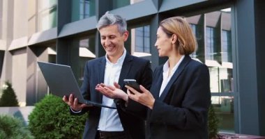Akıllı telefon ve dizüstü bilgisayar kullanan profesyonel bir kadın açık havada yürüme projesini tartışıyor. Elinde bilgisayar olan çekici bir adam iş kadınını dinliyor. Hem gülümsüyor hem de güneşli bir şehirde etkileşim içinde..