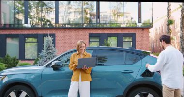 İş kadını dışarıda dizüstü bilgisayarla çalışırken işadamı elektrikli arabayı şarj ediyor. Çevre dostu teknoloji ve modern yaşam tarzı. Yavaş çekim